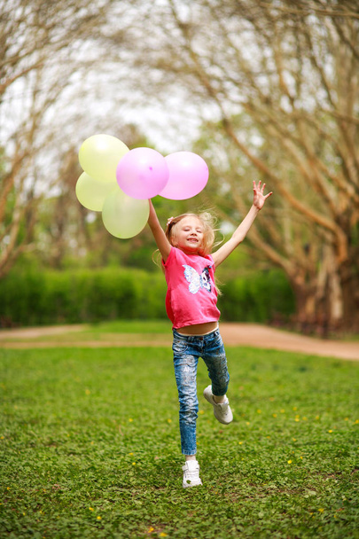 Menina feliz com balões pulando no parque da cidade comemorando o verão
 - Foto, Imagem