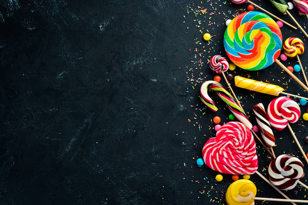 Colorful candies and lollipops. On a black stone background. Top view. free copying space. - Foto, imagen