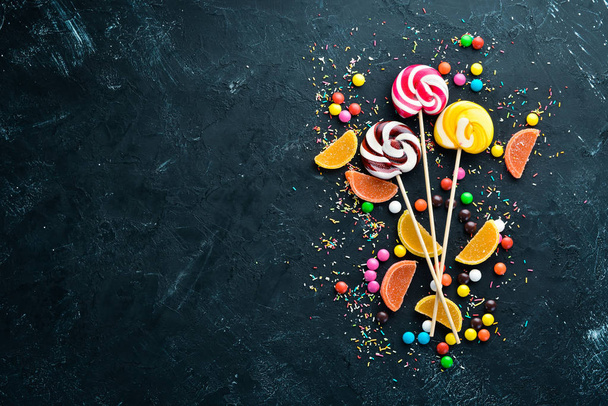 Colorful candies and lollipops. On a black stone background. Top view. free copying space. - Foto, afbeelding