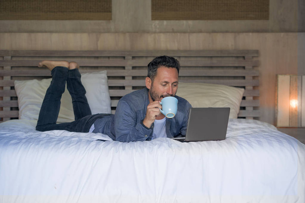 interior portrait of young attractive and happy man at home working relaxed on bed with laptop computer smiling cheerful in freelance networking business success - Foto, afbeelding