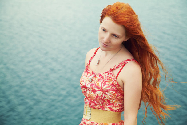 романтическая рыжая молодая женщина в платье на берегу моря
 - Фото, изображение