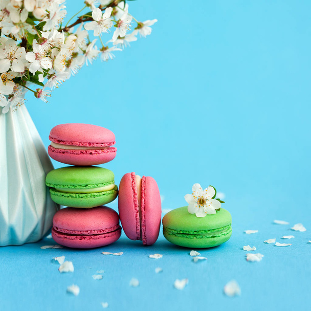 Cherry flowers in blue vase and pink gift box and french colorful macaroons on blue background. - Foto, afbeelding
