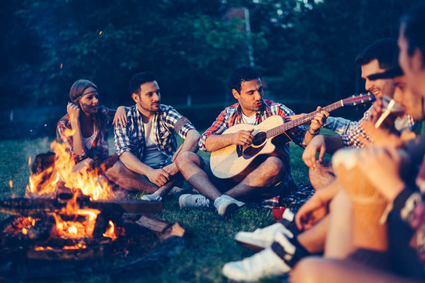 Friends enjoying music near campfire at night - Фото, зображення