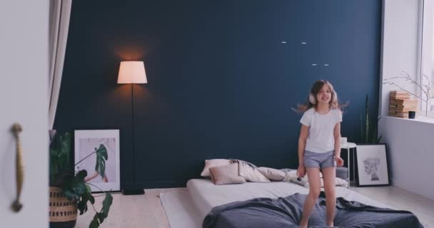 Portrait of a little girl listening to the music with the headphones and dancing on her parents bed. Concept: Music, freedom, happiness - Footage, Video