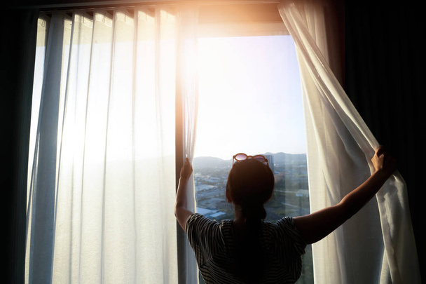 Beautiful woman is opening the curtain at the window in the morn - Foto, Bild