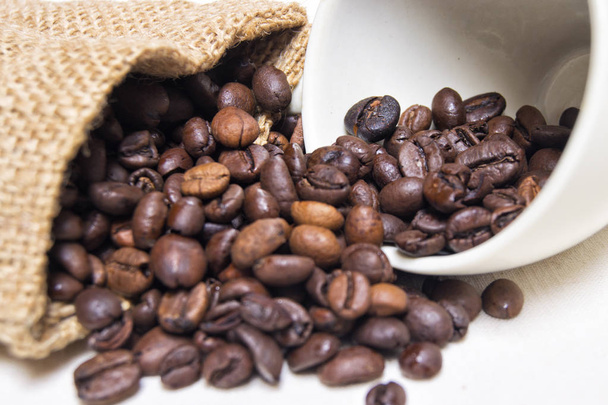 生の織物と白い磁器のコーヒーカップのローストコーヒー豆 - 写真・画像
