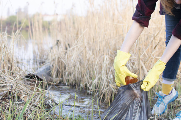 Девушка убирает мусор, бросает пластиковую бутылку в мусорный мешок
 - Фото, изображение
