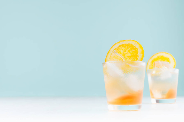 Čerstvé pomeranče koktejl v pořezané sklenici s alkoholem, pomerančové kostky s ledem na měkkém moderním pastelovém zeleném pozadí. - Fotografie, Obrázek
