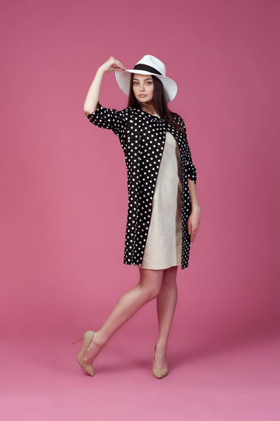 Beautiful young woman in elegant beige dress, polka dot jacket and summer hat. Girl posing on a pink background. - Zdjęcie, obraz