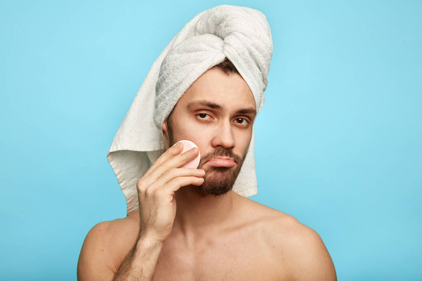 sad guy in bad mood using a cotton disk to apply a lotion - Foto, Bild