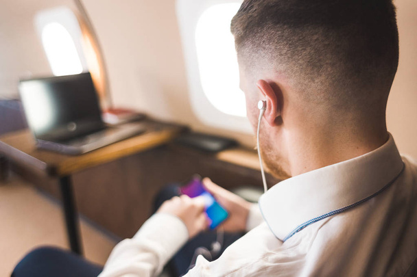 Genç ve başarılı iş adamı dinleniyor ve özel iş uçağının koltuğunda oturmuş müzik dinliyor. - Fotoğraf, Görsel