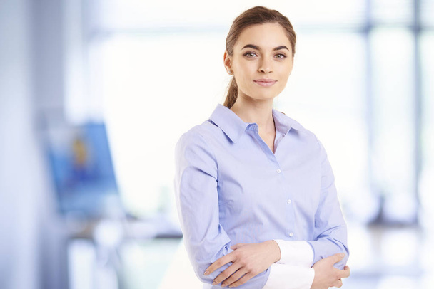 Retrato de una hermosa joven mujer de negocios usando camisa mientras está de pie con los brazos cruzados en la oficina
.  - Foto, imagen