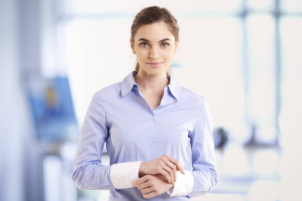Portrait shot of beautiful young businesswoman wearing shirt while standing with folded arms in the office.  - Foto, imagen