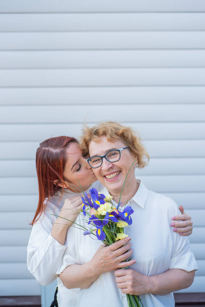 Adult daughter gives flowers to her mother outside, in the courtyard of the house. Spending time together, celebrating at home on weekends. Mothers Day. Warm intergenerational relationships - Photo, Image
