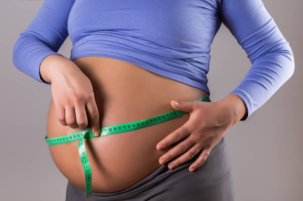 Obrázek těhotné ženy, která měří žaludek na šedém pozadí. - Fotografie, Obrázek