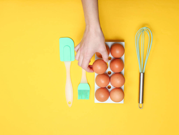 Frauenhand, die Hühnerei aus dem Eierfach auf gelbem Hintergrund nimmt. Kulinarisches Konzept, Küchensilikon, Minimalismus - Foto, Bild