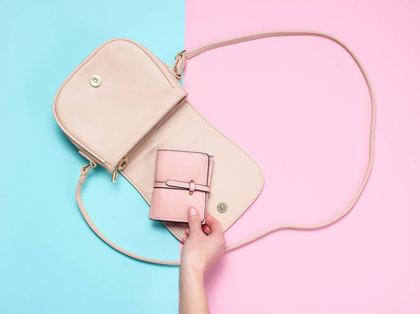 Ženská ruka bere koženou peněženku ze sáčku na pastelové pozadí. Pohled shora, plochý ležel, minimalismus - Fotografie, Obrázek