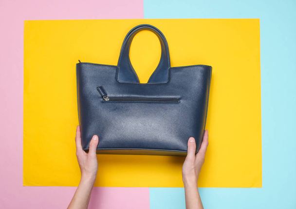Kadın elleri renkli bir kağıt arka plan üzerinde bir deri çanta tutun, üst görünümü, minimalizm - Fotoğraf, Görsel