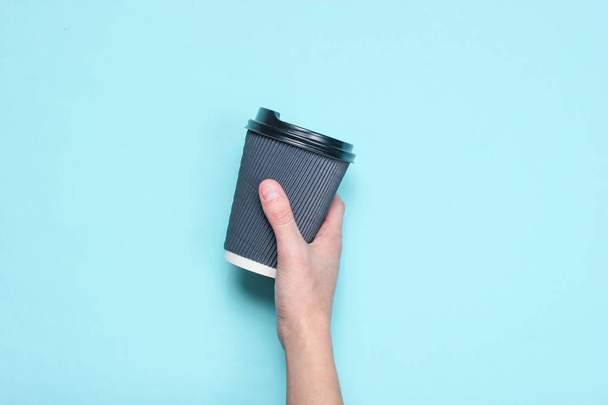 Mano femminile che tiene contenitore di caffè di carta nera su sfondo blu pastello. Vista dall'alto. Minimalismo
 - Foto, immagini