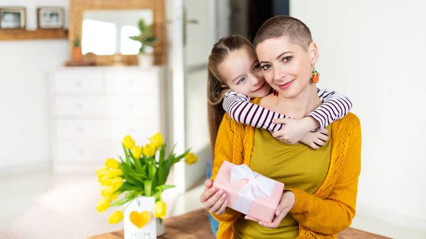 Happy Mother's Day or Birthday Background. Adorable young girl surprising her mom, young cancer patient, with bouquet with present. Family celebration concept. - Foto, Imagen