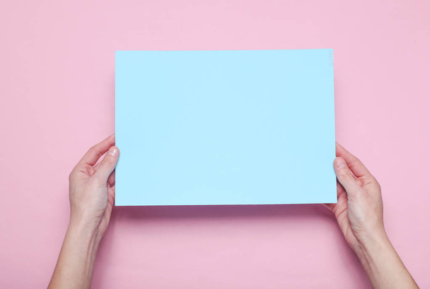 Жіночі руки тримають синій аркуш паперу на рожевому тлі. Вид зверху. Макет, простір для копіювання, мінімалізм
 - Фото, зображення