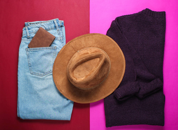 Rovinatý a neklouzáně pletený svetr, módní modré džíny, klobouk a další příslušenství na červeném růžovém pozadí, vrcholový pohled, minimalismus - Fotografie, Obrázek