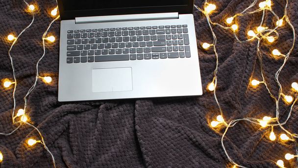 Ноутбук на сером покрывале с гирляндами. Рождественское настроение
 - Фото, изображение