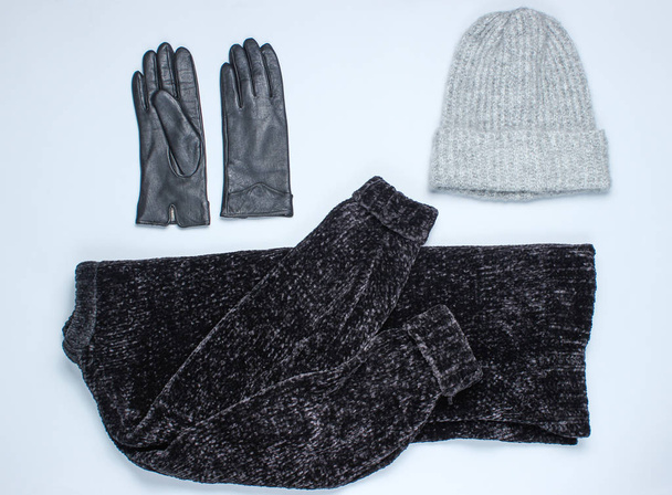 Velor zwarte trui, lederen handschoenen, warme wollen hoed op een grijze achtergrond. Bovenaanzicht. Platte lay stijl - Foto, afbeelding