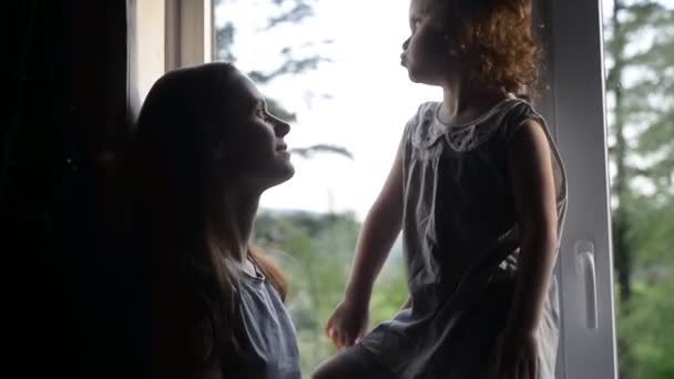 Loving mom laughing caressing touching noses with cute kid daughter sitting on near the window, happy mother and little child girl hugging having fun playing enjoy funny moments good time together - Footage, Video