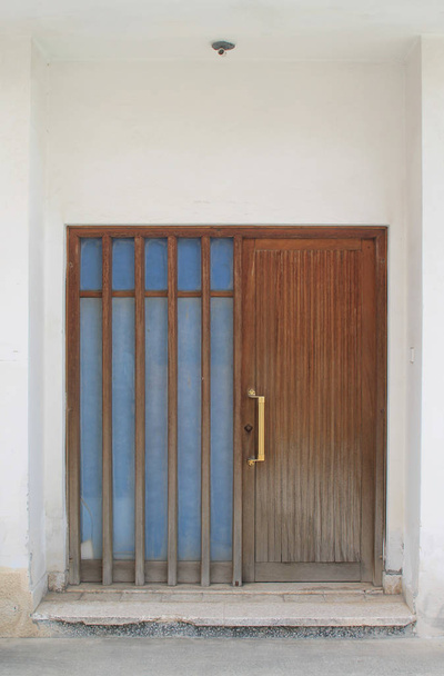 Brązowe drewniane drzwi przednie z uchwytem z mosiądzu w białym kamiennym ścianie - Zdjęcie, obraz