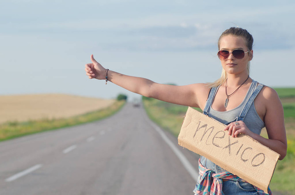 Beautiful girl hitchhiking on the road traveling. - Photo, Image