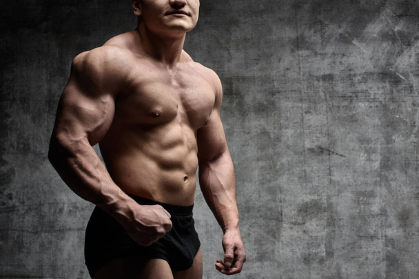 sexy Bodybuilder Mann posiert auf dunklem Hintergrund in schwarzen Shorts. schöner gepumpter männlicher Körper isoliert mit freiem Raum für Werbung - Foto, Bild
