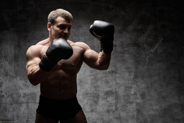 Muscular pumped man boxing in gloves on a black background. Sexy athletic body - Φωτογραφία, εικόνα