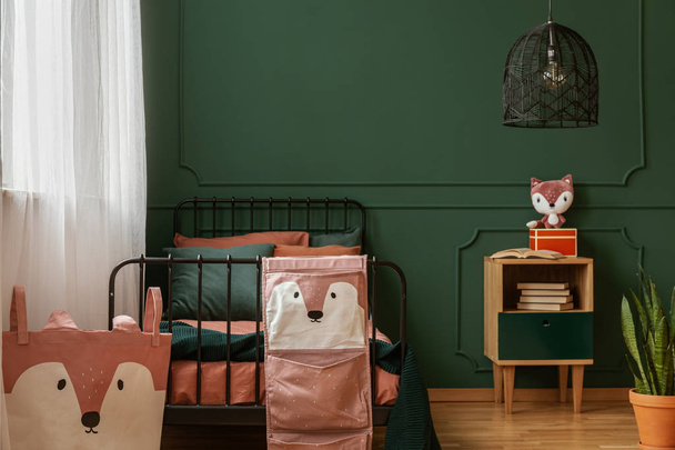 Real photo of black, metal bed standing against dark green wall with molding in a teenager's bedroom interior with fox decorations - Foto, immagini