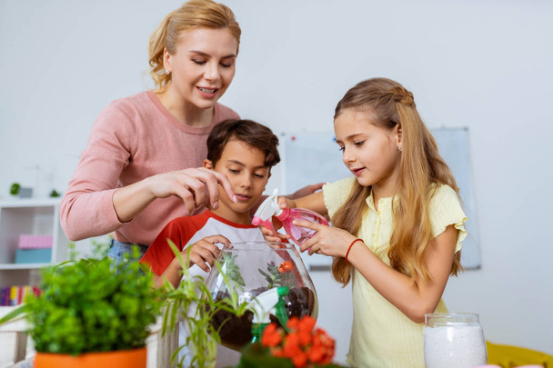 Girl sprinkling water on succulents standing near pupil and teacher - Photo, Image