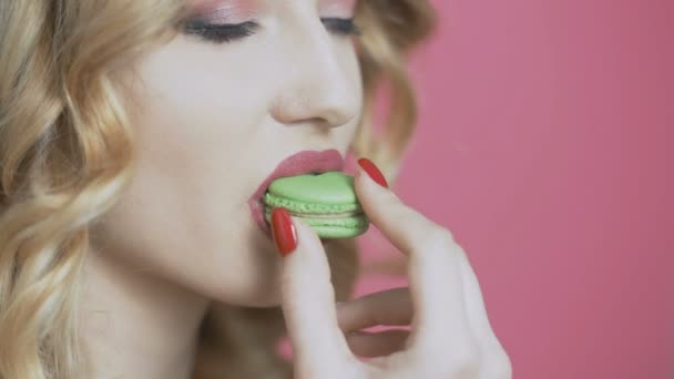 dziewczyna jedzenia apetyczny makaronik na kolorowym tle, młoda kobieta gryzie ciasteczko i to Crumbles, dieta koncepcja, przemysł spożywczy - Materiał filmowy, wideo