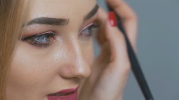 beautiful girl doing makeup in front of the mirror, young woman with picked up hair in a soft hoop powdering the skin of the face with a brush on studio background, the concept of cosmetics and beauty - Filmmaterial, Video