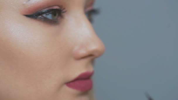 schöne Mädchen Make-up vor dem Spiegel, junge Frau zeichnet Pfeile auf Augenlider mit Applikator auf Studio-Hintergrund, das Konzept der Kosmetik und Schönheit - Filmmaterial, Video