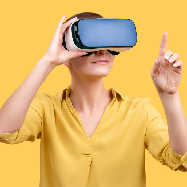 Mujer joven de 30 años usando gafas de realidad virtual. Mujer con gafas VR aisladas sobre fondo amarillo. Concepto de experiencia VR
. - Foto, Imagen