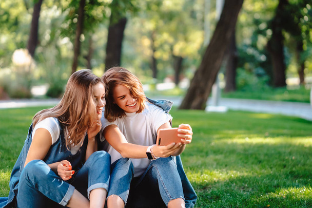 Δύο γυναίκες φίλη κρατώντας κινητό τηλέφωνο ενώ κάθονται σε ένα γρασίδι - Φωτογραφία, εικόνα