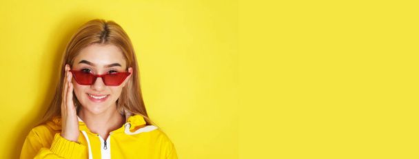 Beautiful girl in yellow jacket and red glasses looking to the camera. - Foto, Imagen