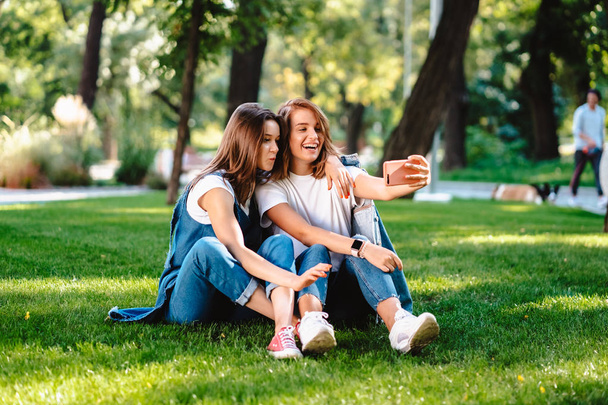 Two female friend sitting in the park have a rest take a selfie - Fotografie, Obrázek