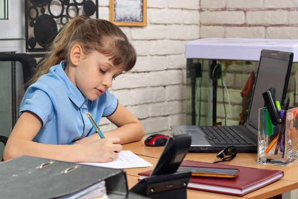 Ένα κορίτσι οκτώ ετών δουλεύει σε ένα τραπέζι σε ένα γραφείο. - Φωτογραφία, εικόνα