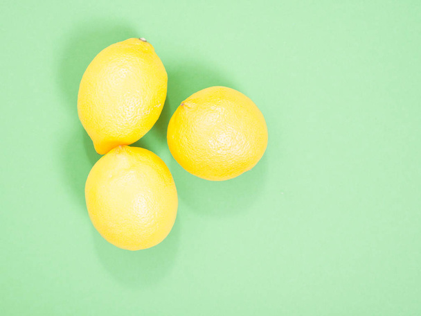 three yellow lemons on a green background. - 写真・画像