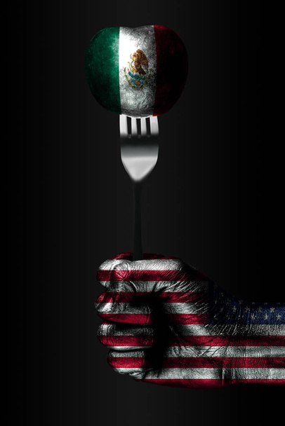 Une main avec un drapeau américain dessiné tient une fourchette, sur laquelle se trouve une balle avec un drapeau mexicain dessiné, un signe d'influence, de pression, d'adhérence et d'anecxie
. - Photo, image