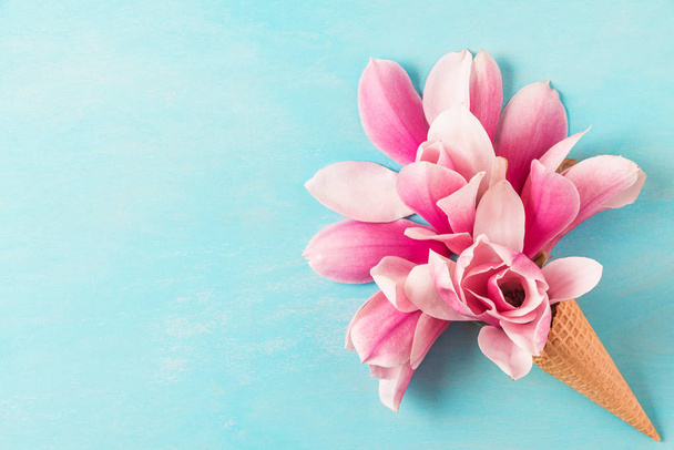 ramo de flores de magnolia rosa en cono de helado sobre fondo azul. fondo de la boda. Acostado. vista superior
 - Foto, imagen