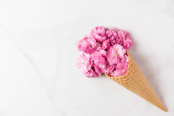 pink cherry blossoms flowers bouquet in ice cream cone on white marble background. wedding background. Flat lay - Foto, afbeelding