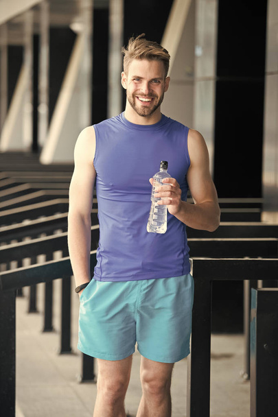 Sporty nutrition concept. Man athlete hold plastic bottle care hydration body after workout. Refreshing vitamin drink. Athlete drink water after training. Man athletic appearance holds water bottle - Foto, afbeelding