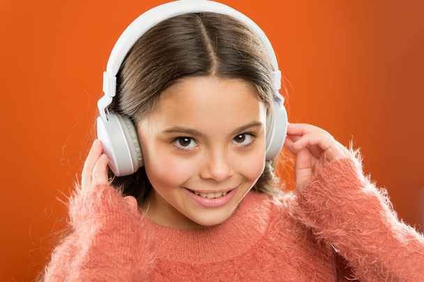 Menina bonito criança usar fones de ouvido ouvir música. Miúdo ouvir música fundo laranja. Música recomendada com base no interesse inicial. Diz-me o que ouves e eu digo-te quem és.
 - Foto, Imagem