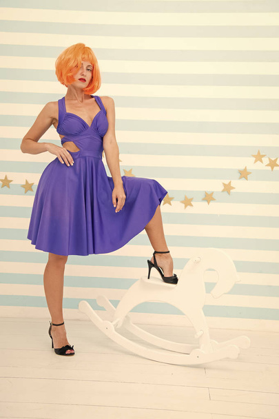 Tame anyone she wants. Comic and humorous concept. Woman playful but confident mood having fun. Never too late to tame horse. Girls power in beauty. Lady red ginger wig blue dress and rocking horse - Фото, зображення